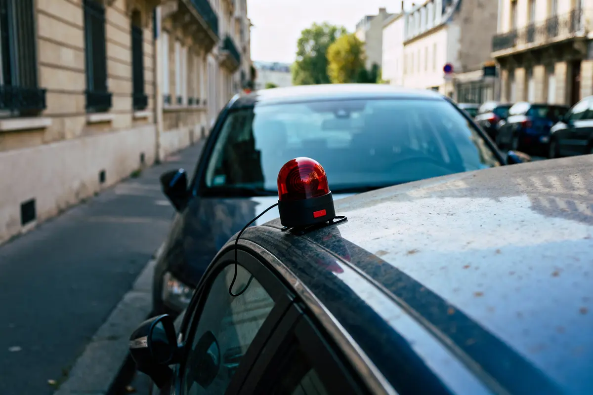 Voitures garées en rue, gyrophare rouge sur le toit d'une voiture, bâtiments en arrière-plan.