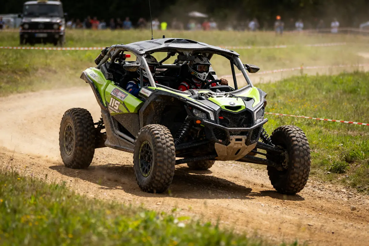 Deux personnes conduisent un buggy vert en course tout-terrain sur un chemin poussiéreux.