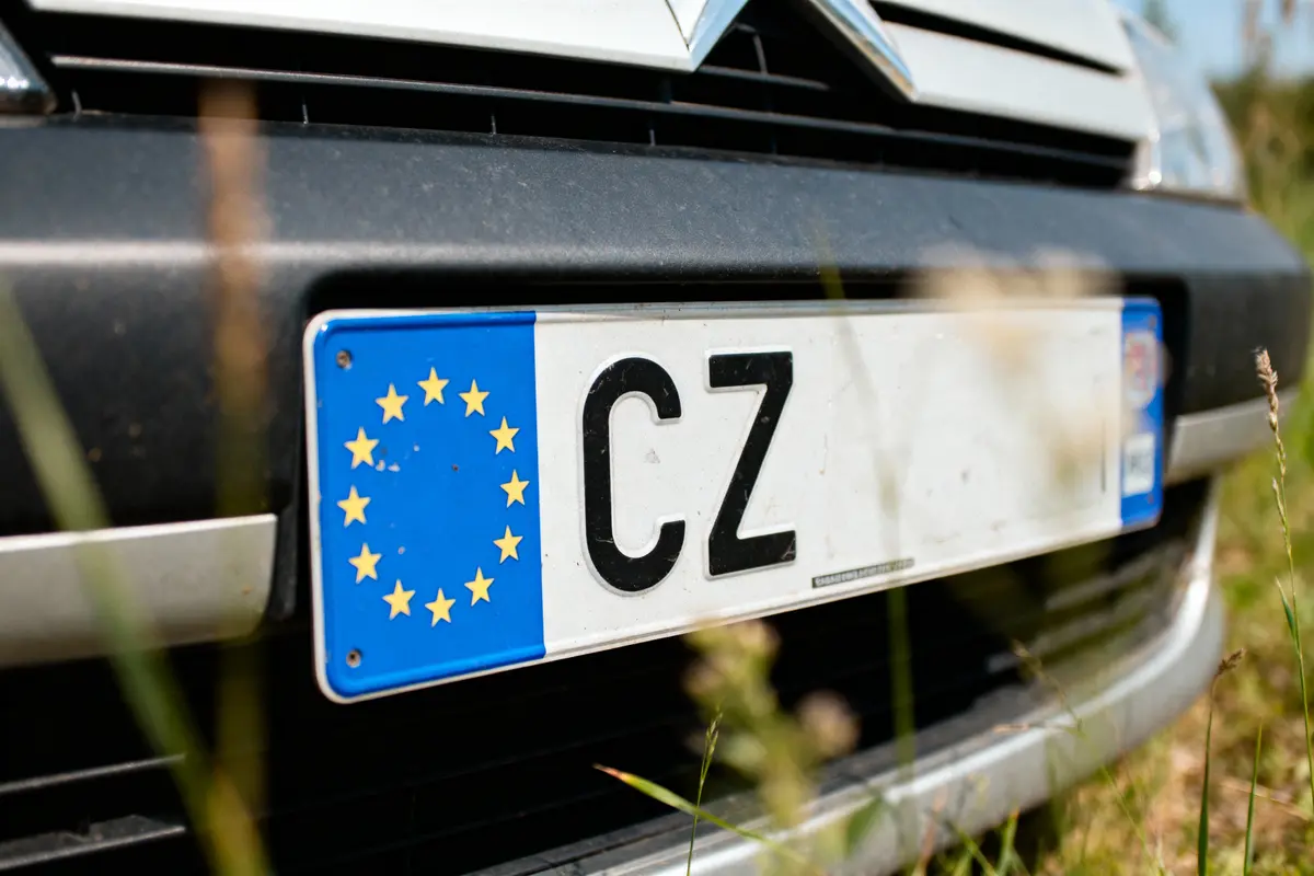 Plaque d'immatriculation de voiture tchèque avec symbole européen sur pare-chocs avant, herbe floue au premier plan.