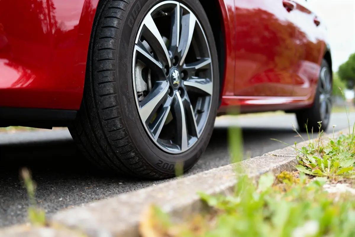 Roue de voiture rouge stationnée sur la route, près d'un trottoir avec herbe.