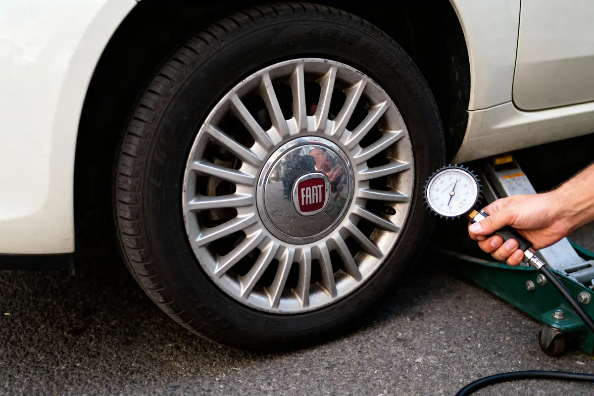 Main vérifiant la pression du pneu d'une voiture Fiat avec un manomètre.