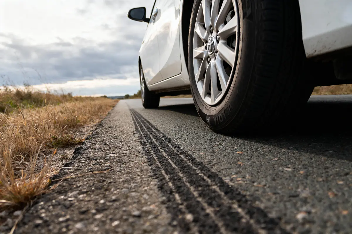 Voiture blanche sur route de campagne avec traces de pneus, ciel nuageux en arrière-plan.