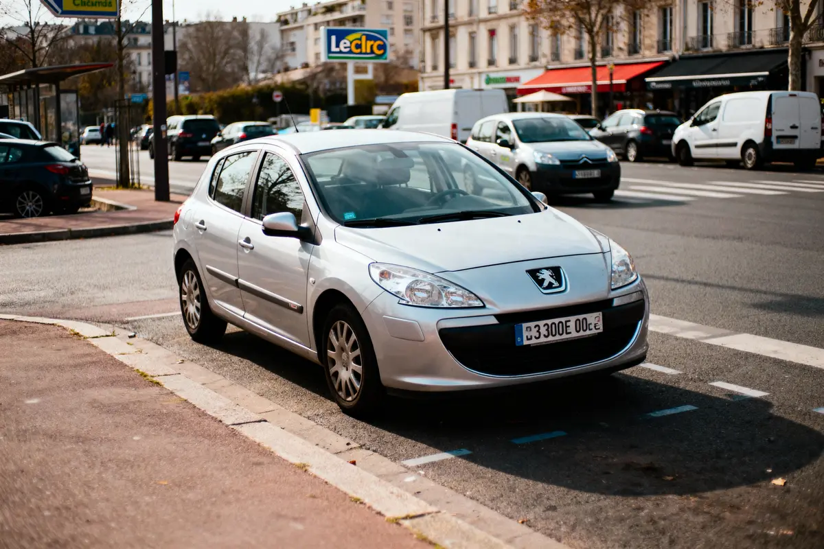 Voiture Peugeot grise stationnée en ville devant un magasin Leclerc, avec circulation en arrière-plan.