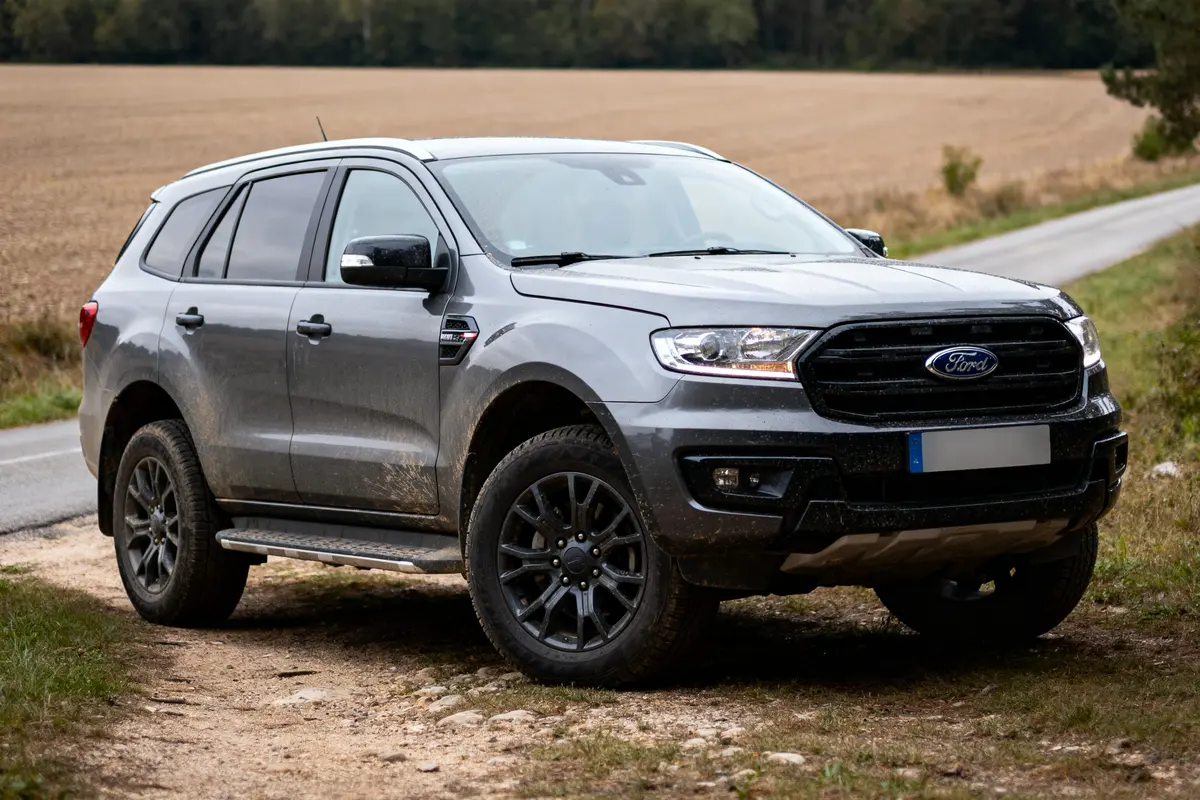 SUV gris Ford stationné sur chemin de terre, près d'un champ et d'une route.