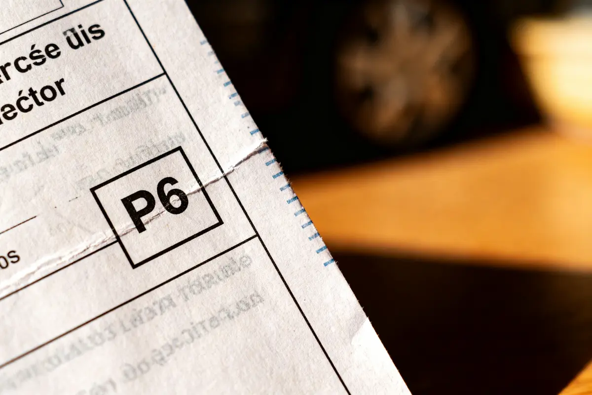 Papier avec code "P6" imprimé, coin éclairé, texte partiellement lisible en arrière-plan flou.