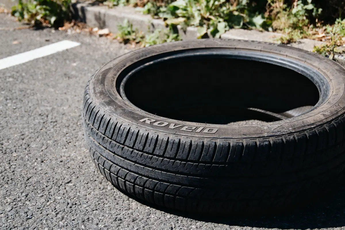 Pneu usagé marqué "Rovelio" sur asphalte, près de bordure végétalisée.