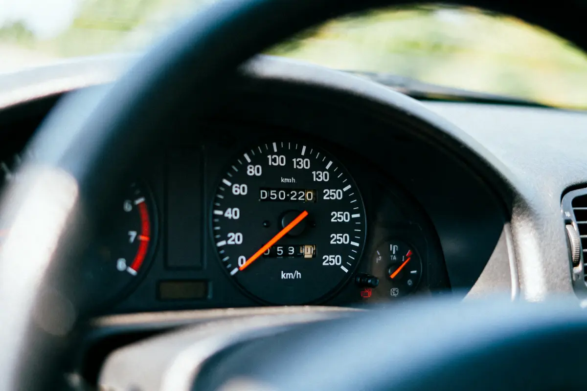 Tableau de bord de voiture avec compteur de vitesse et jauge de carburant visibles, éclairé par le soleil.