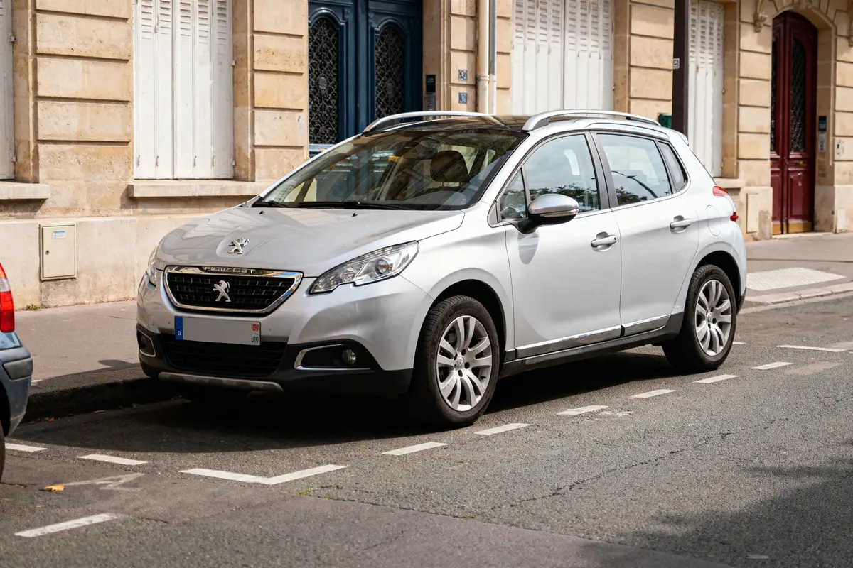 Voiture Peugeot blanche stationnée devant un bâtiment en pierre avec fenêtres et portes. Rue urbaine.