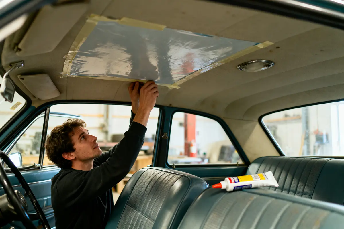Homme répare le plafond intérieur d'une voiture vintage avec ruban adhésif et colle.