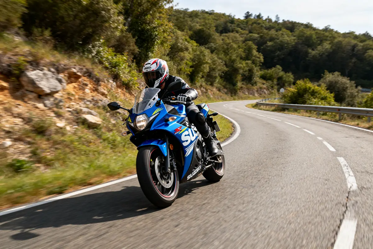 Motard en Suzuki bleu GRSX roulant sur route sinueuse en pleine nature verdoyante