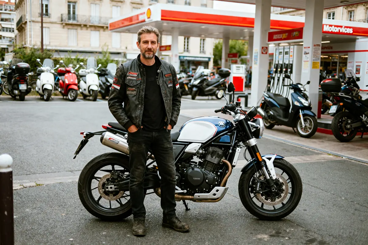 Un homme pose avec une moto devant une station-service Motoservices.