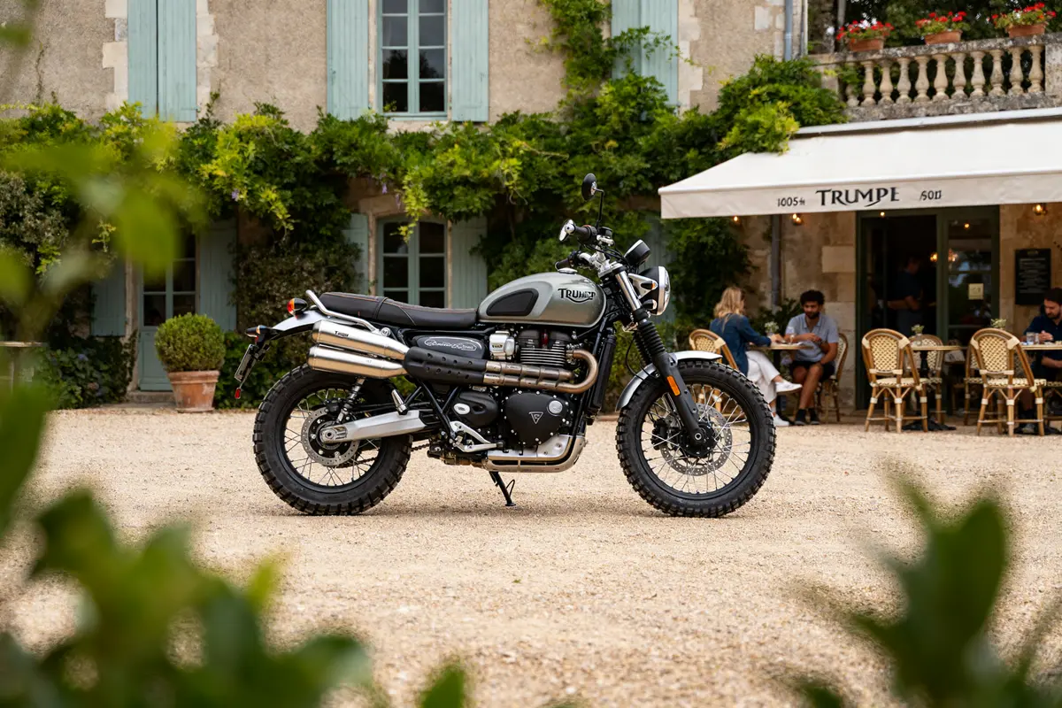 Triumph Scrambler 900 garée devant un café pittoresque avec des personnes assises en terrasse