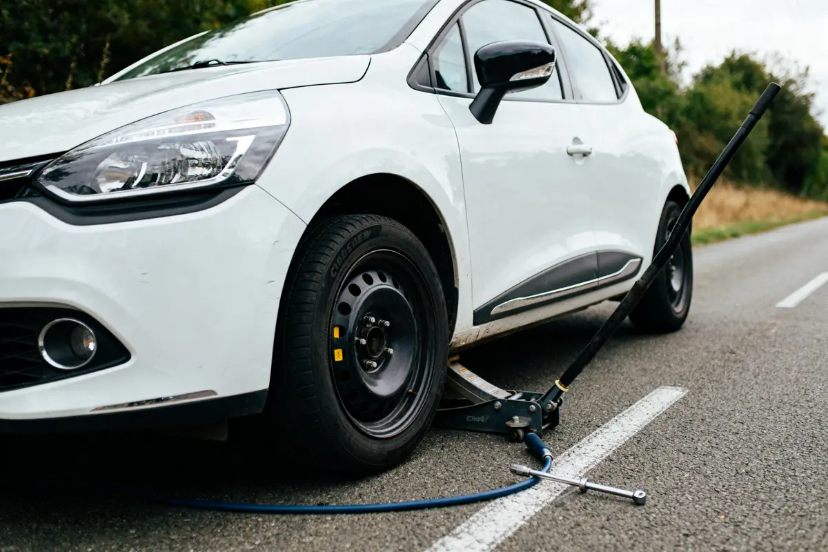 Clio 4 blanche avec vérification de pression de pneu sur route avec vérin et compresseur