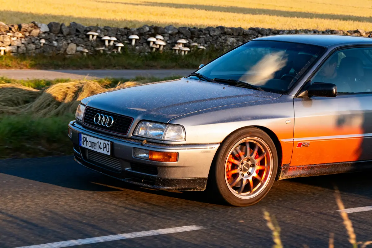 Audi RS2 Avant en mouvement sur route de campagne, jantes rouges distinctives.