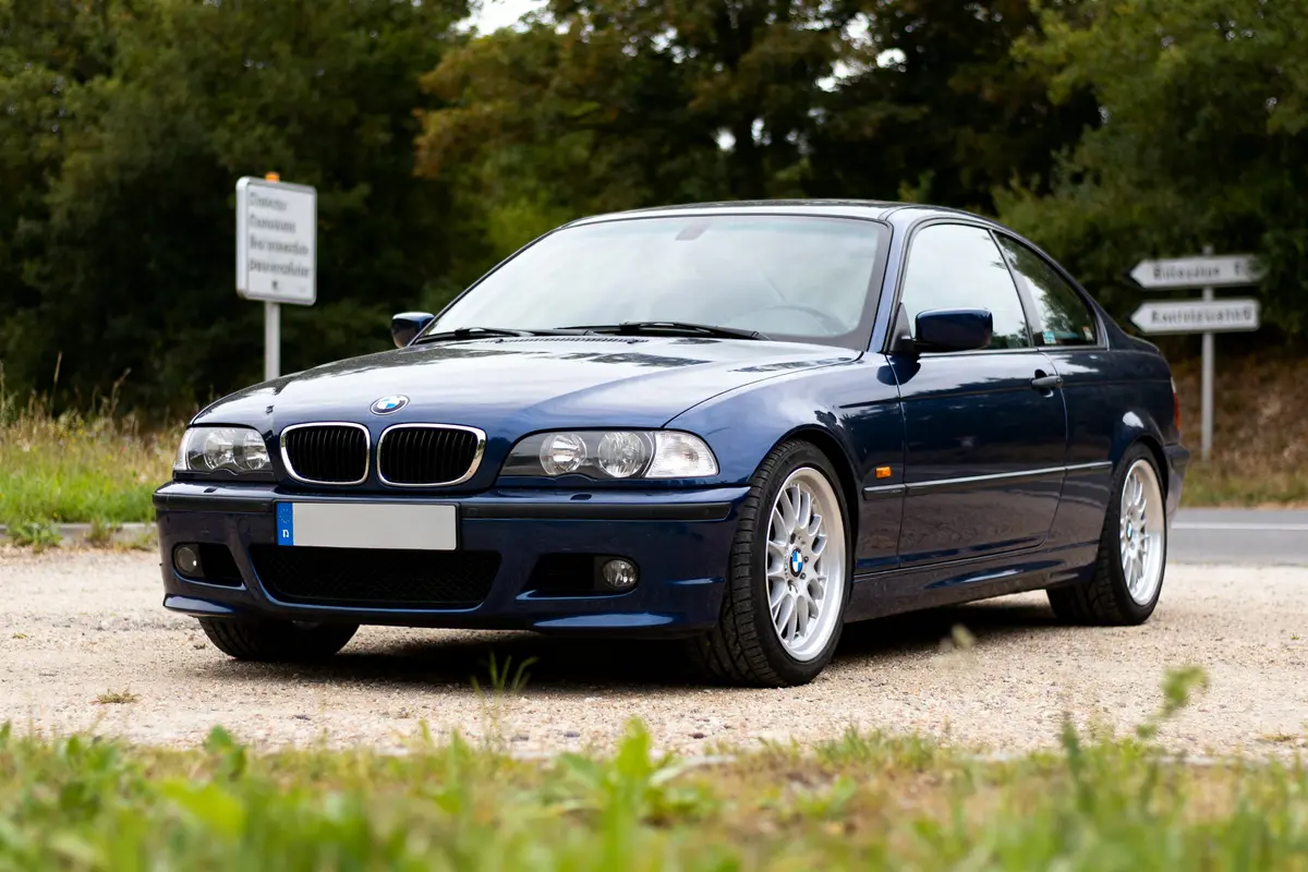 Voiture bleue BMW E46 garée sur un chemin de gravier devant des arbres
