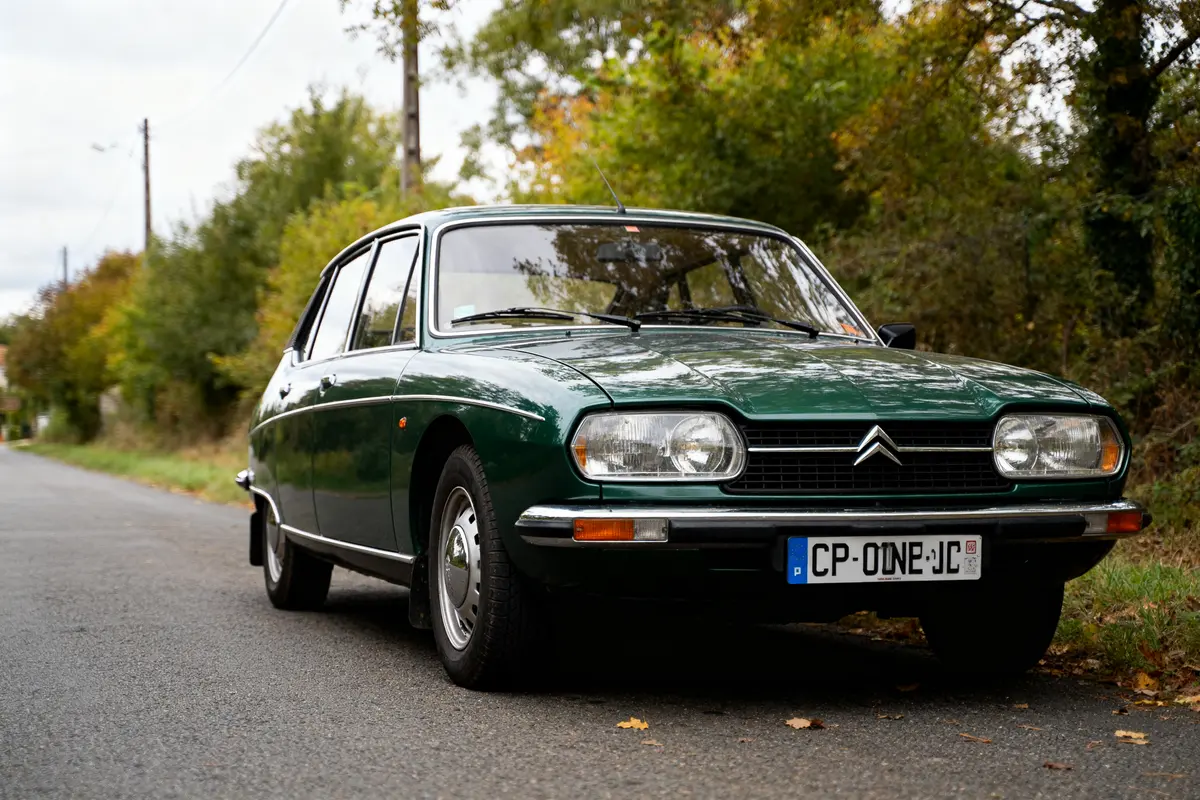 Voiture vintage verte Citroën GS stationnée sur une route bordée d'arbres