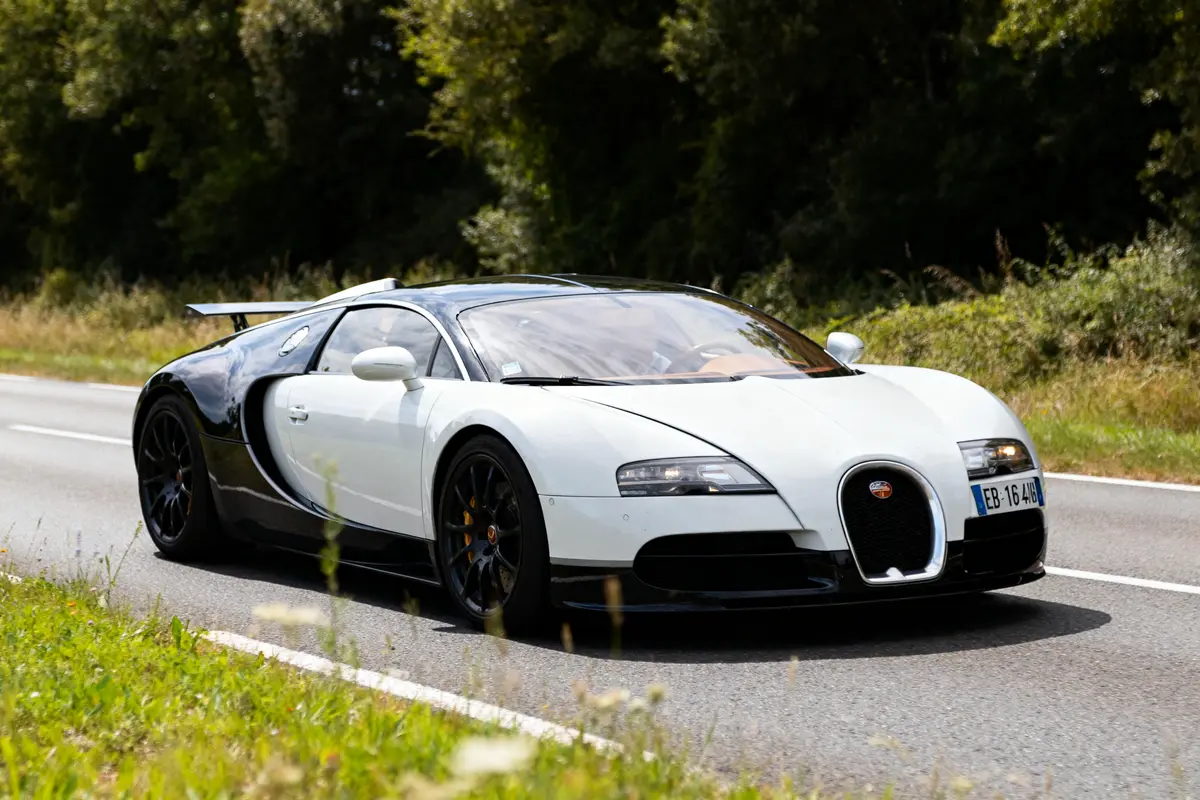 Voiture sportive EB 16.4 Veyron blanche et noire roulant sur route bordée d'arbres