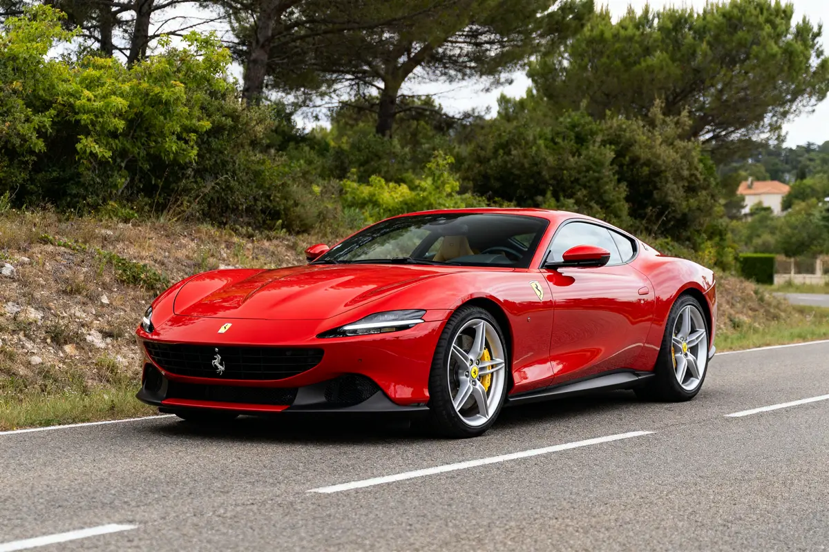Ferrari Roma rouge garée sur une route bordée d'arbres et de verdure luxuriante