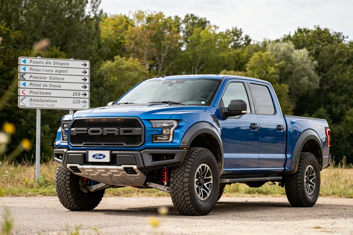 Pickup bleu Ford Raptor cab garé sur chemin devant panneau directionnel et forêt