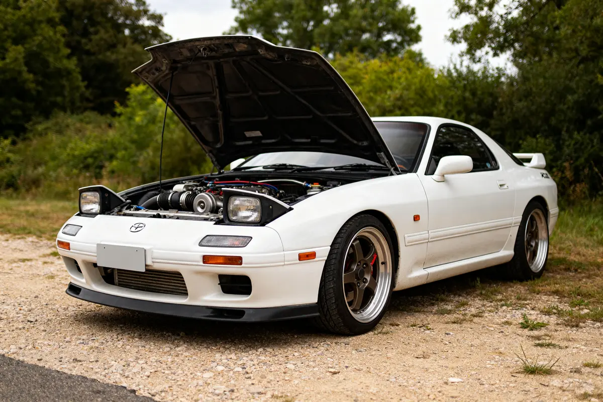 Mazda RX7 coupé blanc capot ouvert sur route avec moteur visible
