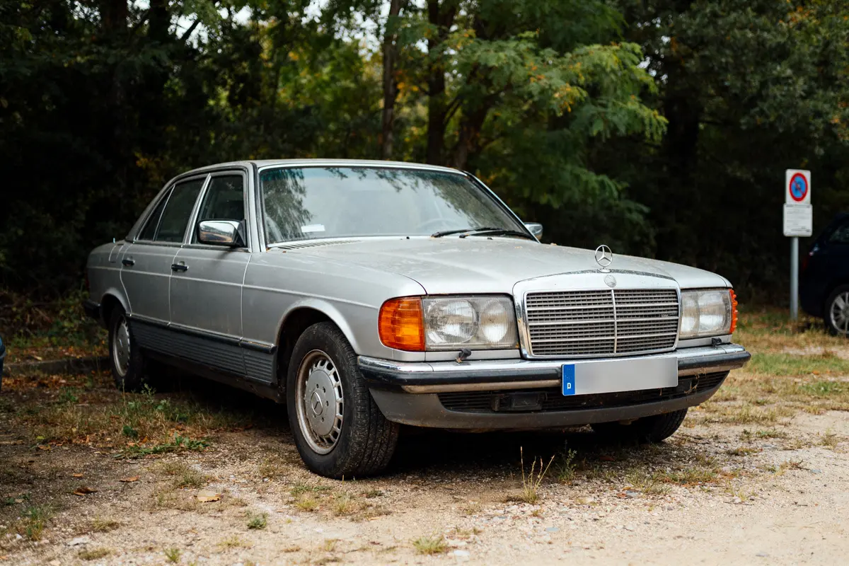 Mercedes ancienne grise stationnée en extérieur près d'arbres et d'un panneau de signalisation