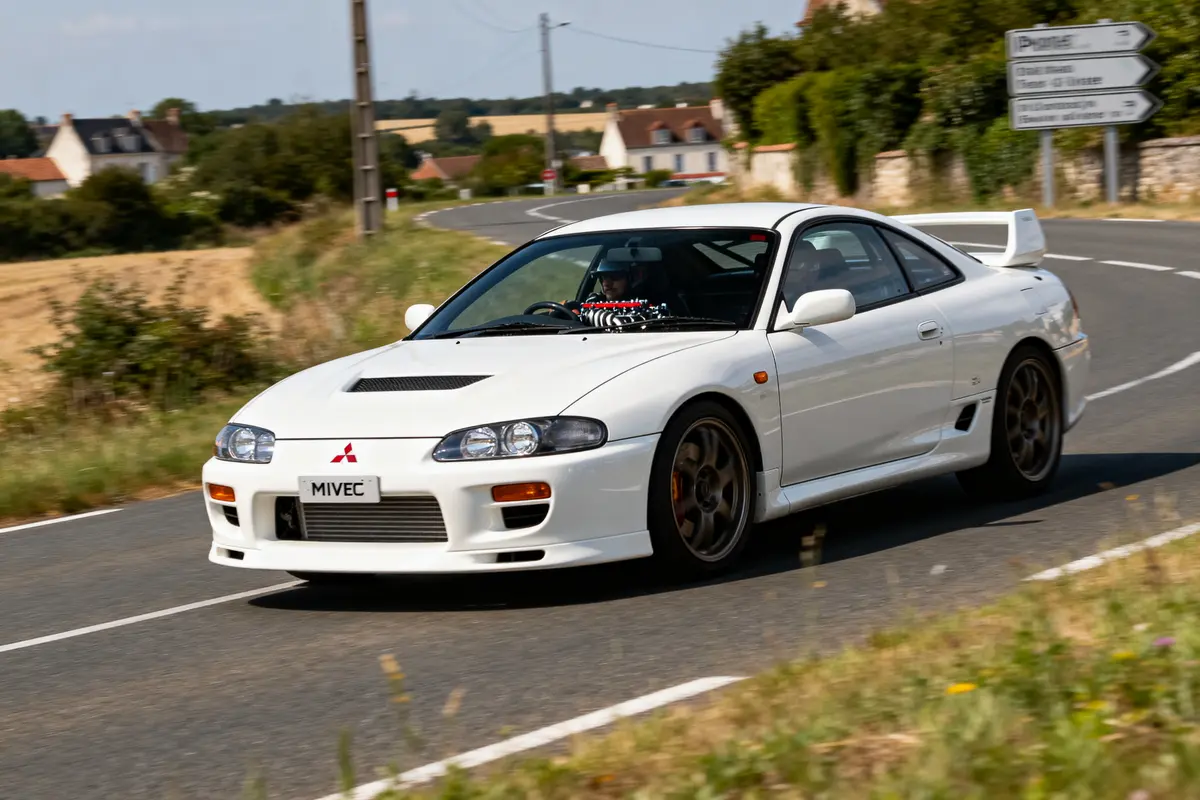 Voiture sportive blanche Mitsubishi FTO coupé sur route de campagne en plein virage