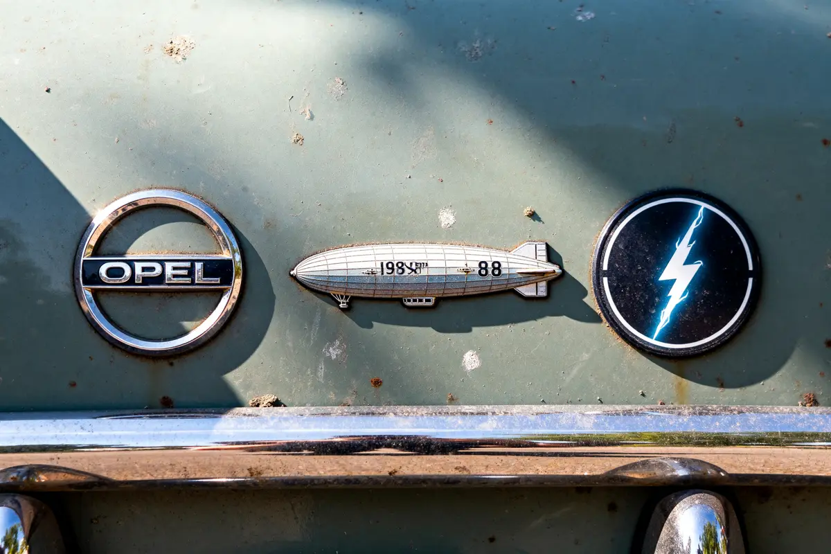 Trois emblèmes sur voiture ancienne avec logo Opel, dirigeable et insigne éclair.
