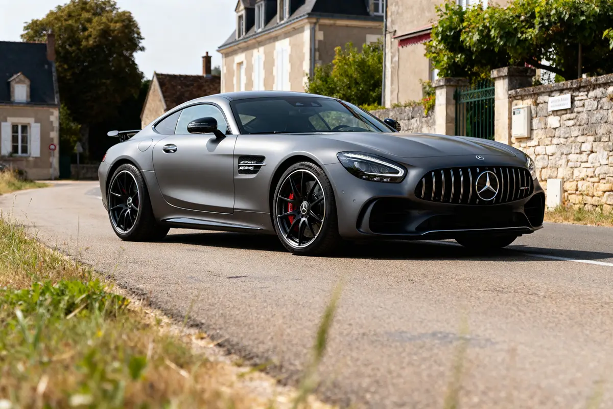 Voiture grise Mercedes-AMG Gran Turismo garée devant maisons en pierre sur route rurale