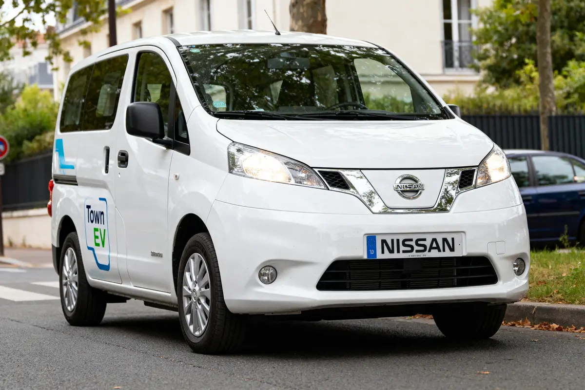 Un utilitaire Nissan blanc électrique conduit en zone résidentielle avec logo Town EV visible
