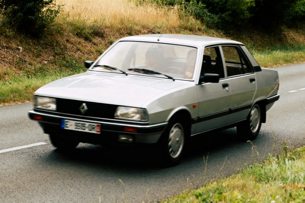 Voiture Renault 18i grise roulant sur une route de campagne avec végétation