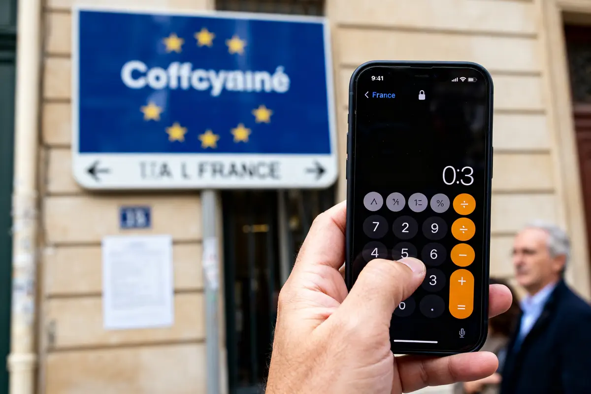 Main tenant un smartphone montrant un calculateur de moyenne devant un panneau européen