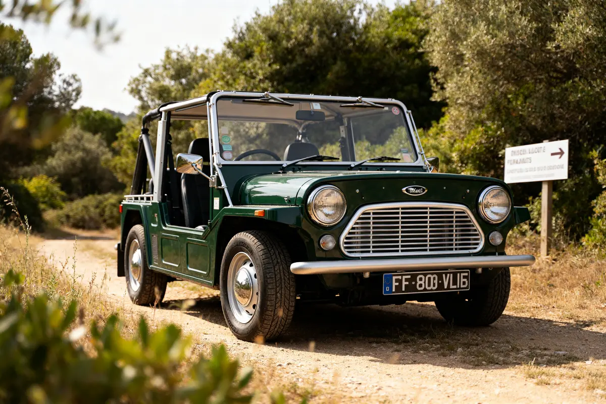 Mini Cooper Moke verte sur chemin rural ensoleillé avec végétation en arrière-plan